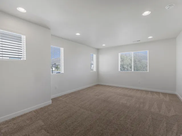 Recessed lighting, multiple windows with blinds, and neutral carpet flooring