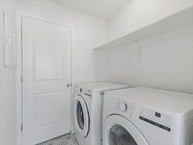 Laundry area featuring a built-in shelf, white paneled door, and patterned floor tile