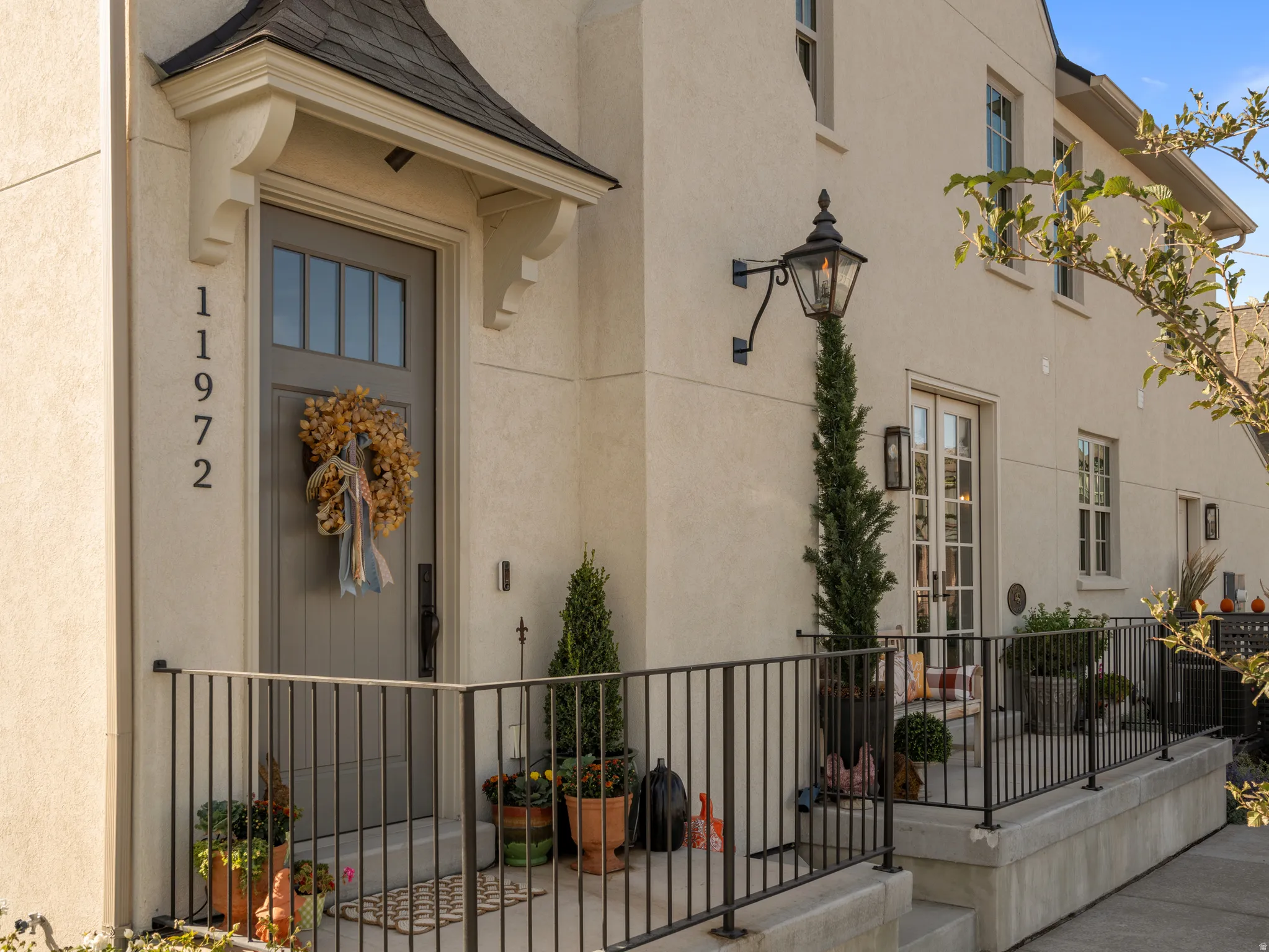Stucco exterior with a peaked entry canopy, a panel-style front door with upper lites, an ornate wall-mounted lantern, and a wrought iron porch railing