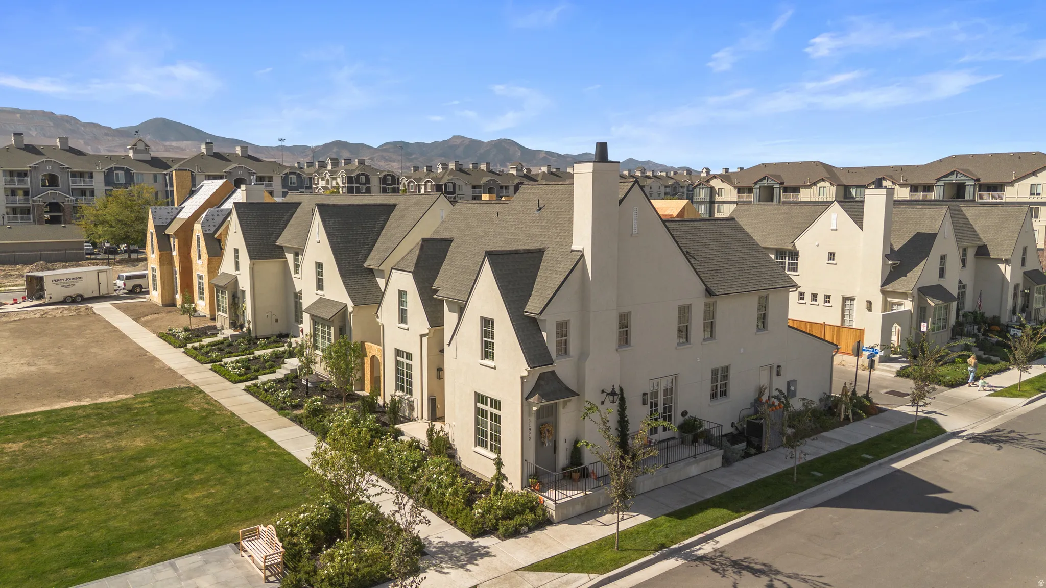 Multiple-gabled roofline, light-colored stucco exterior, prominent chimneys, established landscaping, and a well-defined sidewalk