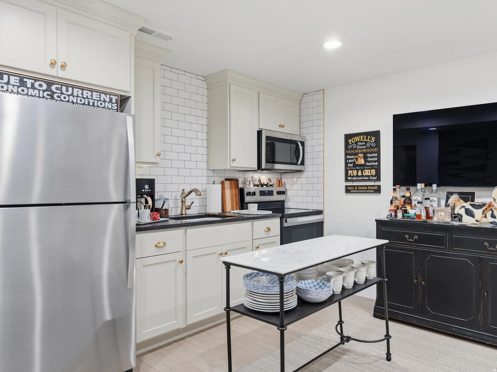 Kitchen featuring stainless steel appliances, white subway tile backsplash, light-toned cabinetry with gold-tone hardware, and dark countertops