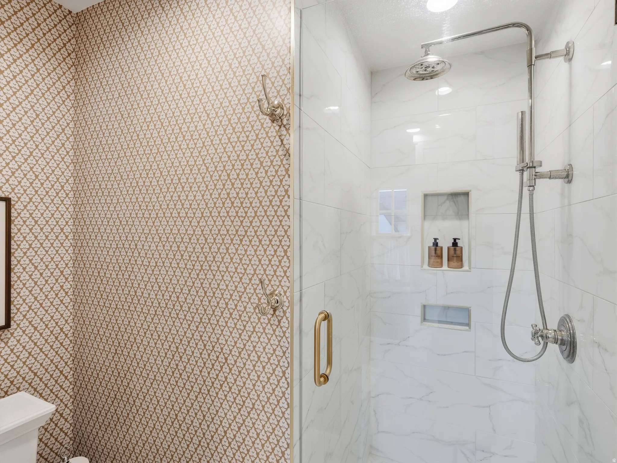 Glass-enclosed shower with white tiled walls, a rain showerhead, a handheld shower fixture, and a built-in shower niche