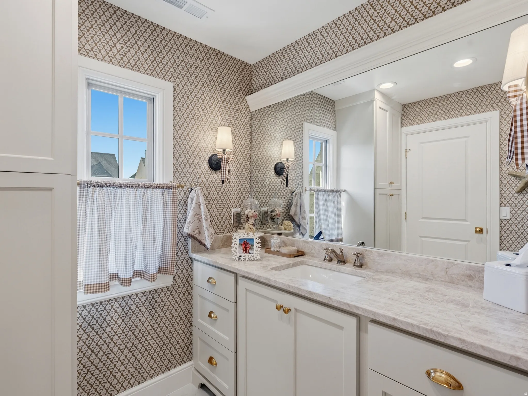 Built-in vanity with light-toned countertop, dual sconce lighting, integrated sink, and white cabinetry with brass hardware