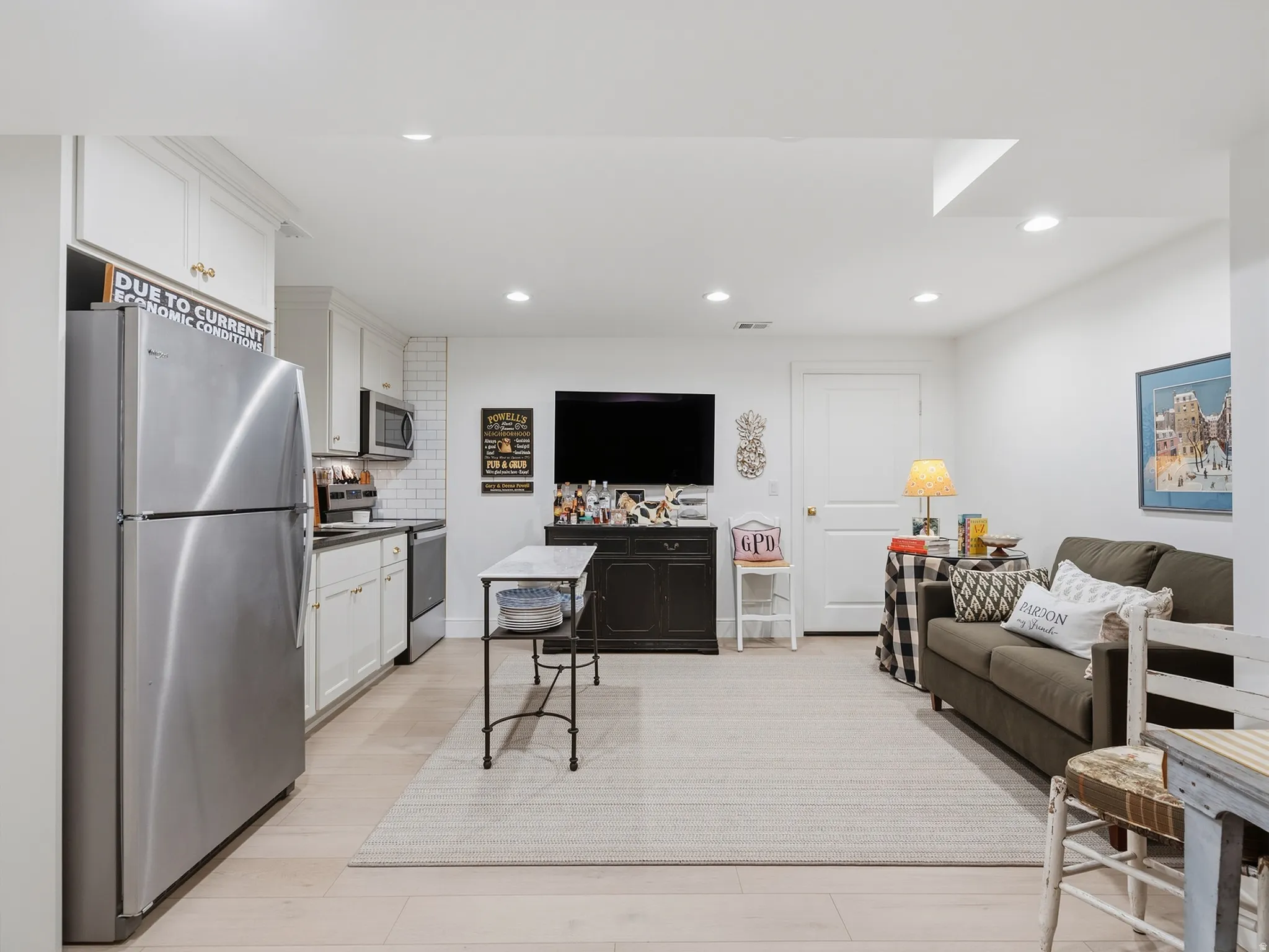 Open-concept living space with wood-finish flooring, recessed lighting, and a full kitchen featuring stainless steel appliances, white cabinetry, and subway tile backsplash