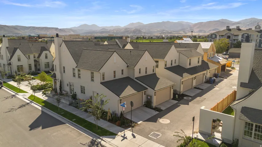 Contemporary townhomes featuring light-toned exteriors, dark shingle roofs, attached garages, and landscaped front yards
