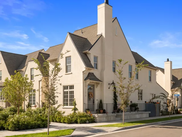 Stucco exterior with multiple gables and dormer windows, featuring a prominent chimney, an entryway portico, and a black wrought iron railing