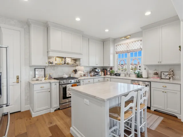 Kitchen featuring wood-finish flooring, light cabinetry, stone countertops, a central island, and stainless steel appliances