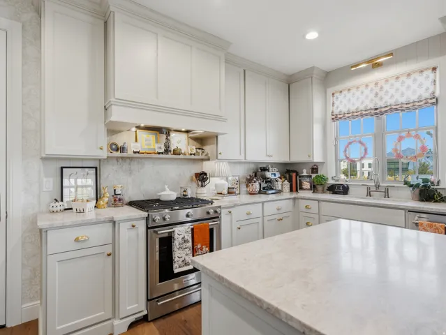 Kitchen featuring white shaker-style cabinetry, a stainless steel range, light-toned countertops, a patterned backsplash, and a window with a traditional grid pattern