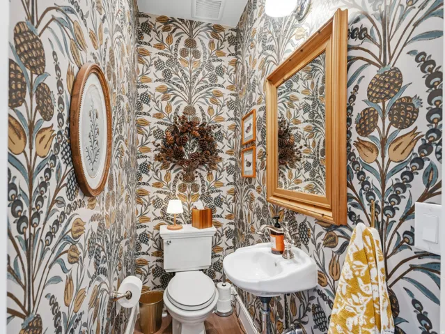 Pedestal sink, wall-mounted mirror with wood frame, patterned wallpaper, and wood-finish flooring