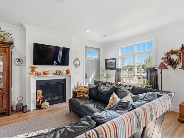 Living area featuring a fireplace with a white mantel, recessed lighting, wood-finish flooring, a multi-pane window, and a door with an upper glass panel