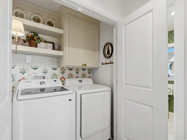 Dedicated laundry room featuring white front-load washer and electric dryer, decorative tile backsplash with botanical motif, custom cabinetry with upper shelving for storage, and recessed lighting throughout