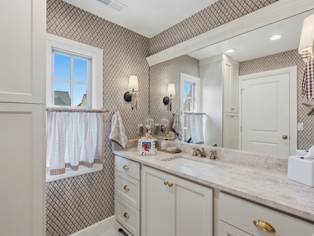 Built-in vanity with light-toned countertop, dual sconce lighting, integrated sink, and white cabinetry with brass hardware