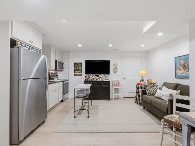 Open-concept living space with wood-finish flooring, recessed lighting, and a full kitchen featuring stainless steel appliances, white cabinetry, and subway tile backsplash
