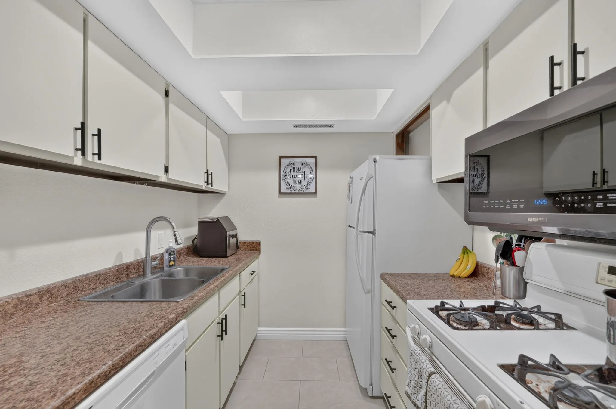 Galley kitchen featuring white cabinetry, speckled countertops, stainless steel sink, tile flooring, and integrated overhead lighting
