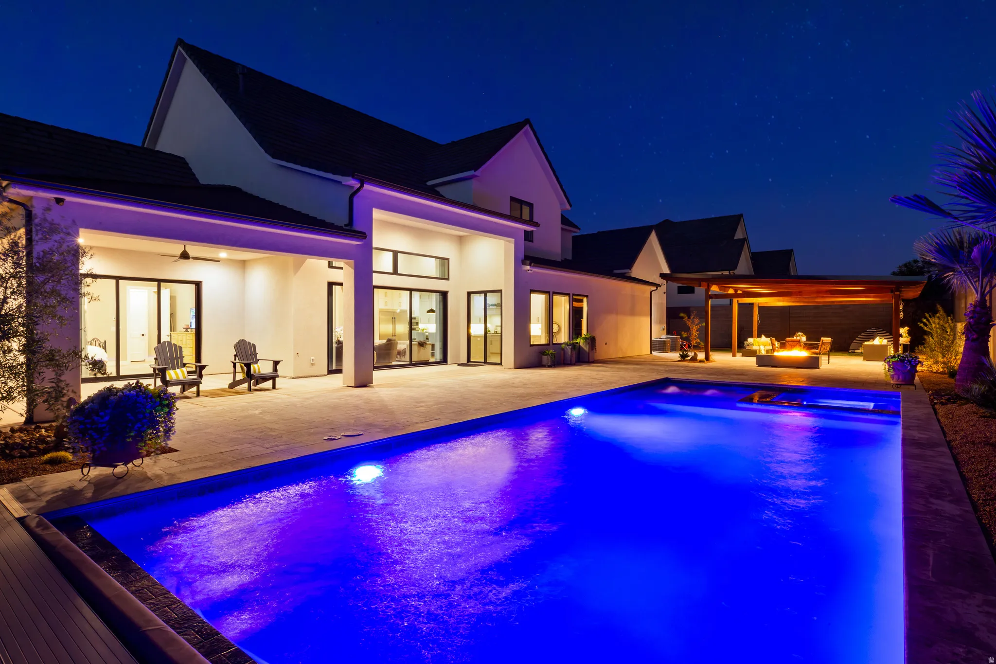 Expansive outdoor living area featuring a rectangular swimming pool, spacious paved patio, covered outdoor lounge, and wood-beam pergola