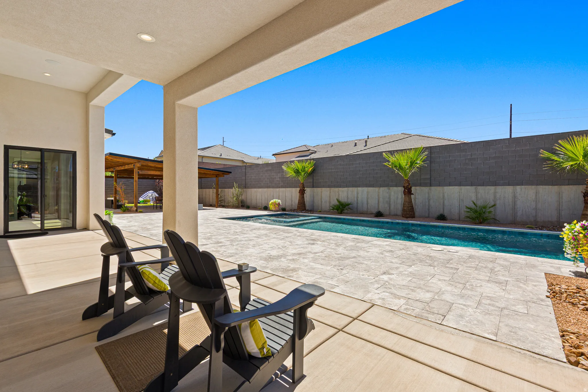 Expansive outdoor living area featuring a covered patio, paved hardscaping, a rectangular swimming pool, and a wooden pergola structure