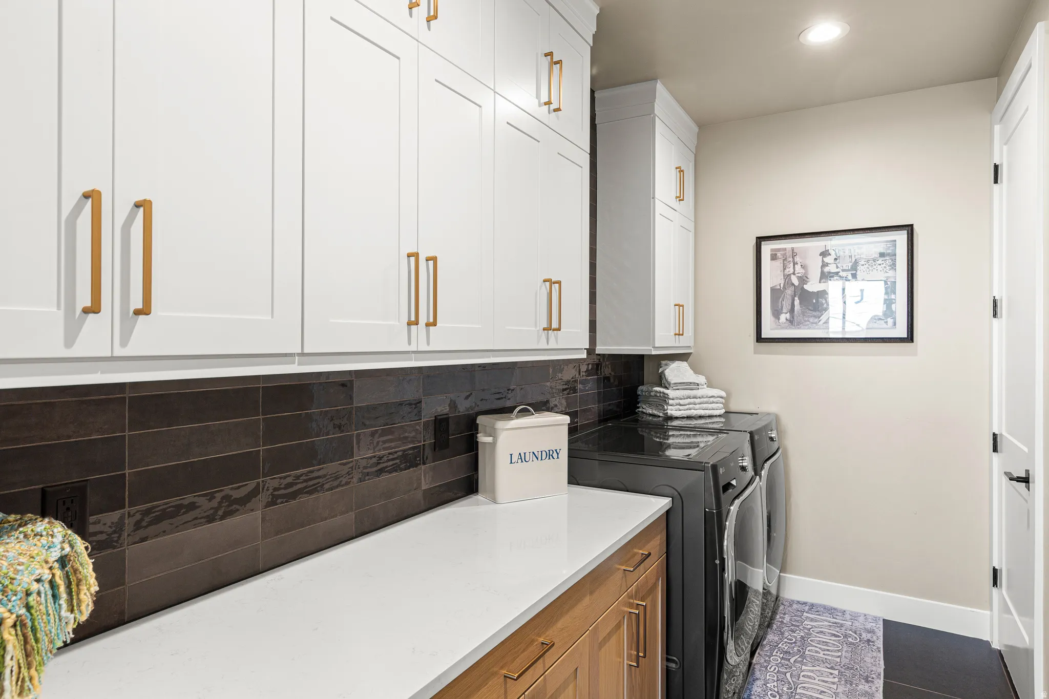 White shaker-style cabinetry with gold-tone hardware, dark subway tile backsplash, light wood-finish lower cabinetry, and recessed lighting