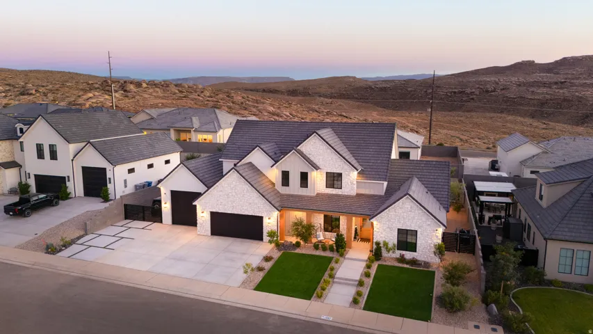 Contemporary white stone exterior with dark-toned roofing and trim, featuring multiple garage bays, a front porch, and manicured landscaping