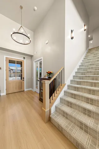 Light wood-finish flooring with a multi-paned wood entry door, high ceilings, and a staircase with plaid carpet and wood railing