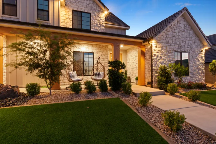 Stone veneer exterior with board-and-batten accents, concrete pathway, gravel landscaping, and artificial turf