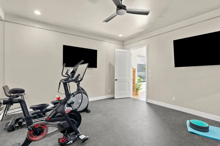 Dedicated exercise room featuring dual wall-mounted televisions, recessed lighting, and a ceiling fan