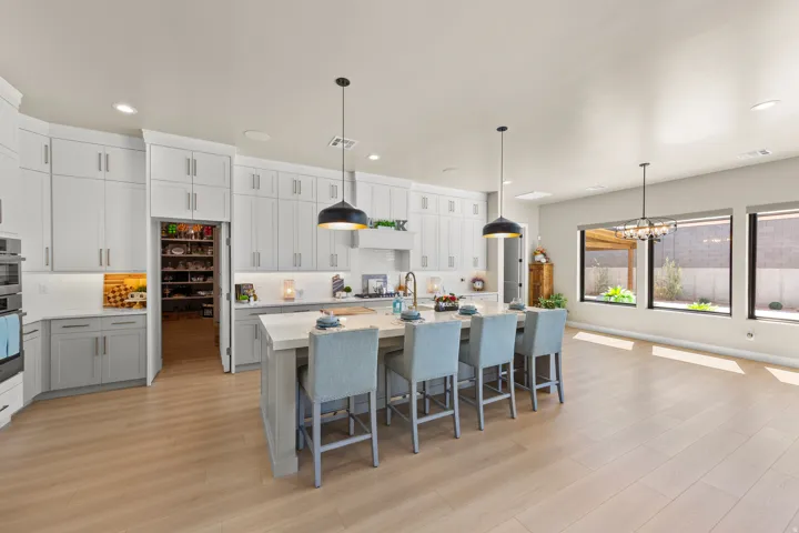 Kitchen featuring an oversized island with seating, extensive cabinetry with integrated pantry, built-in double ovens, and wood-finish flooring