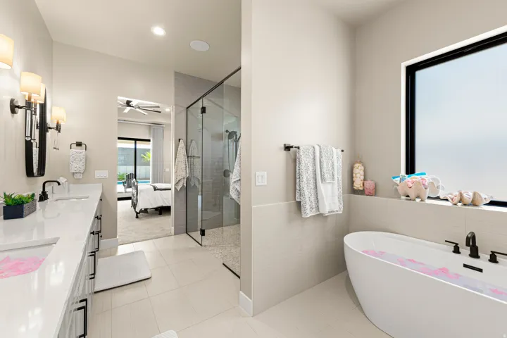 Dual vanity with undermount sinks, frameless glass shower enclosure, freestanding soaking tub, large window, and tile flooring