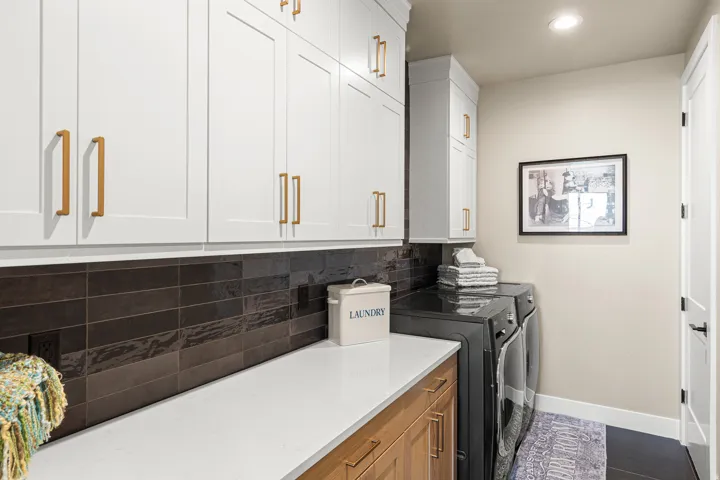 White shaker-style cabinetry with gold-tone hardware, dark subway tile backsplash, light wood-finish lower cabinetry, and recessed lighting