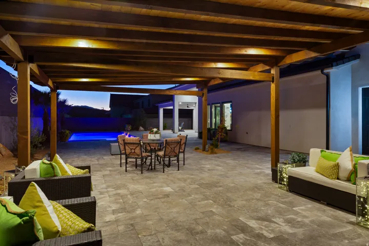 Spacious outdoor living area with a wood pergola, expansive paved patio, built-in swimming pool, and dedicated fire pit