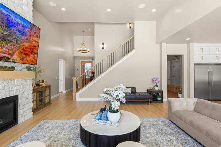 Stone-faced fireplace with a wood mantel, wood-finish flooring, staircase with dark balusters, recessed lighting, and kitchen cabinetry with stainless steel appliances