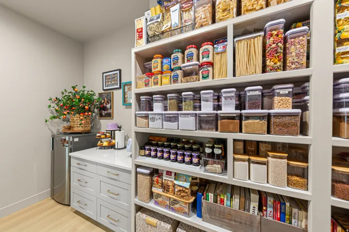 Built-in pantry shelving featuring extensive storage, light wood-finish flooring, white cabinetry with silver hardware, and a solid surface countertop