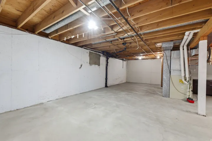 Unfinished basement room with concrete flooring, exposed wood ceiling joists, and concrete walls