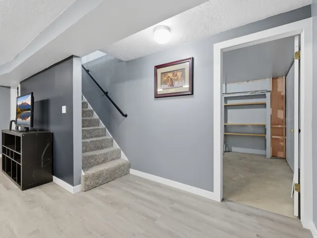 Basement staircase with wood-finish flooring, neutral wall tones, carpeted staircase with handrail