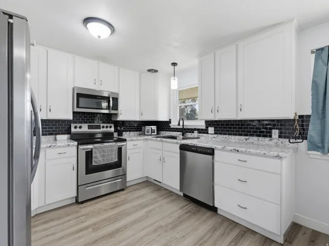 White cabinetry with brushed nickel hardware, stainless steel appliances, black subway tile backsplash, light-toned wood-finish flooring, and light-toned countertops