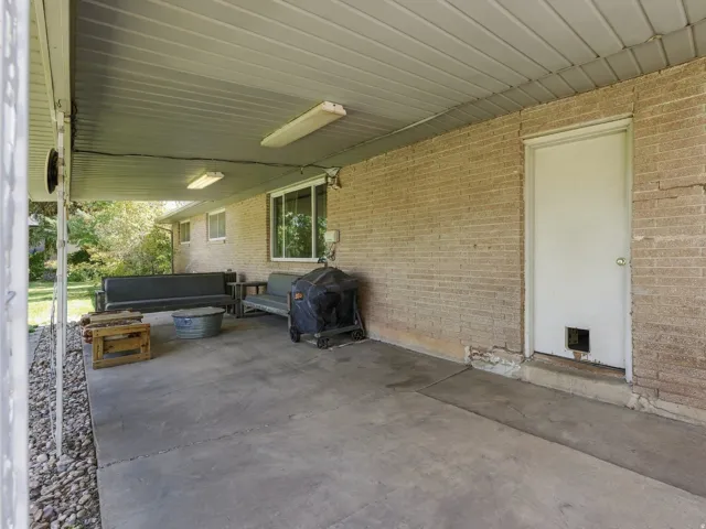 Covered concrete patio with a brick exterior, featuring a white door and an exterior window