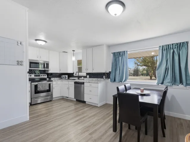 Kitchen with white cabinetry, stainless steel appliances, dark tile backsplash, and light wood-finish flooring