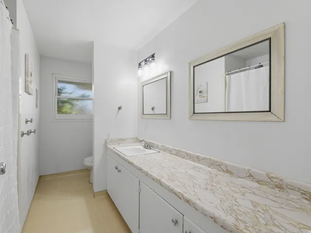 Full bathroom featuring elongated vanity, light-toned countertop, white cabinetry, and two framed mirrors