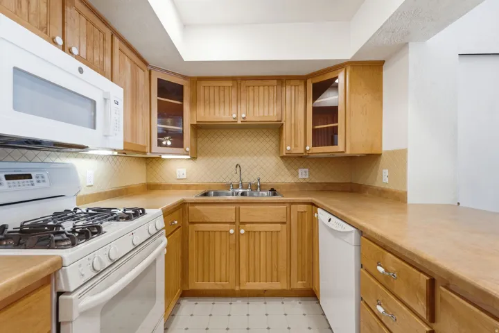U-shaped kitchen featuring light wood cabinetry, a double basin stainless steel sink, tile backsplash, and overhead lighting