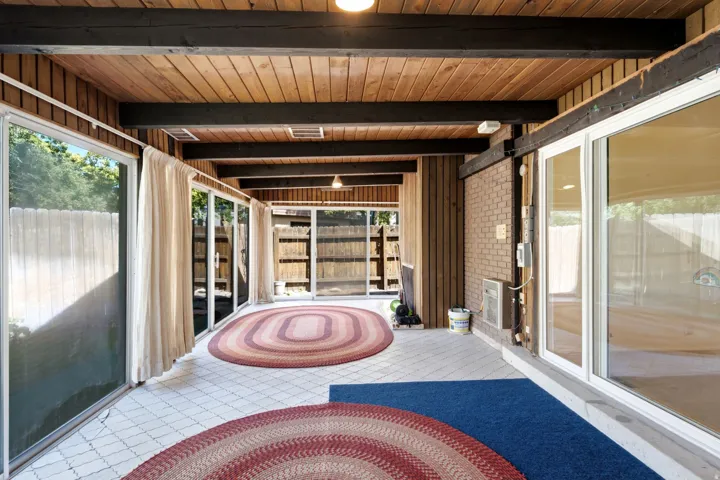 Covered patio with sliding glass doors, exposed wood beam ceiling, wood plank ceiling, and brick wall accents