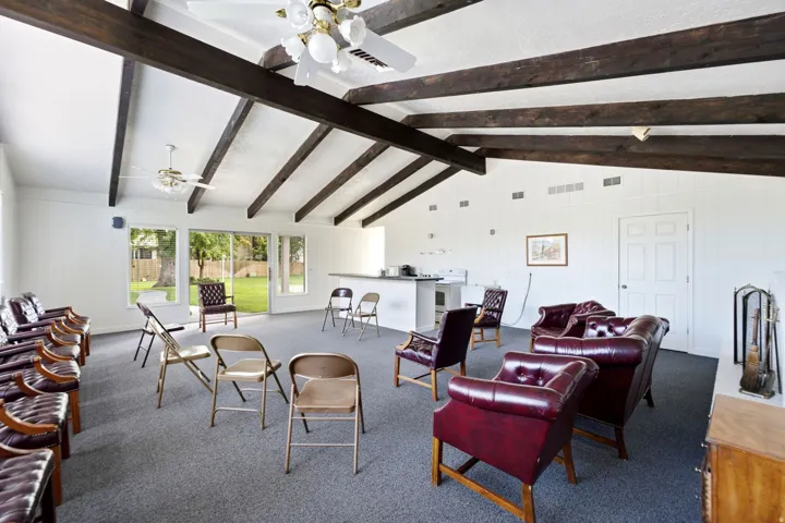 Vaulted ceiling with exposed wood beams, multiple ceiling fans, sliding glass door to the exterior, white paneled walls, and a built-in counter area