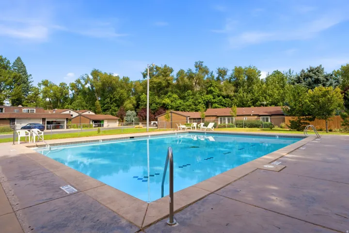 In-ground swimming pool with a concrete surround, stainless steel handrails, and a perimeter fence