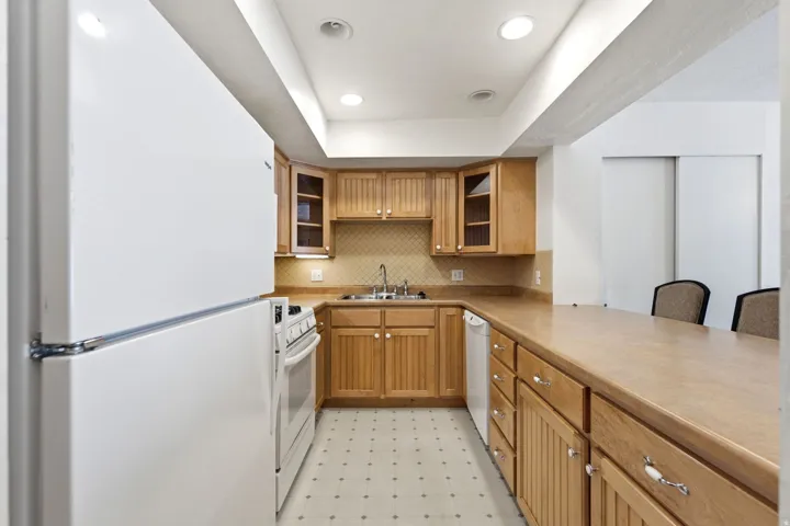 U-shaped kitchen featuring wood cabinetry, integrated white appliances, and recessed lighting