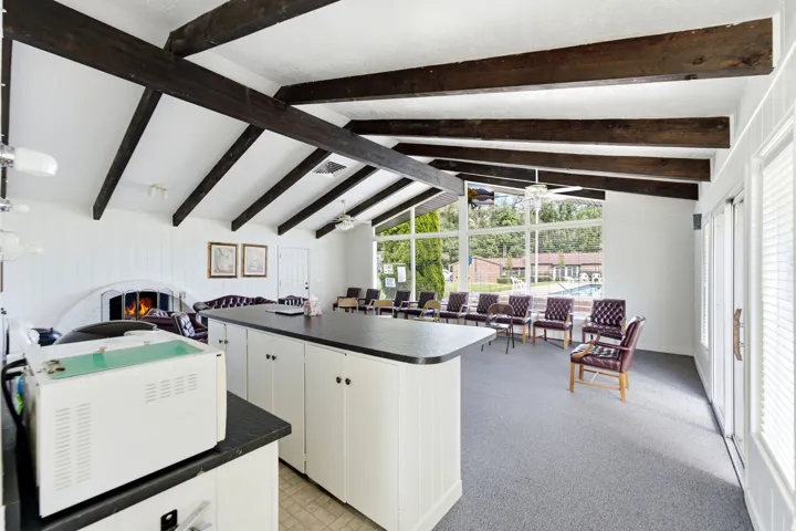 Vaulted ceiling with exposed wood beams, built-in fireplace, large-pane windows, and a built-in counter with cabinet storage