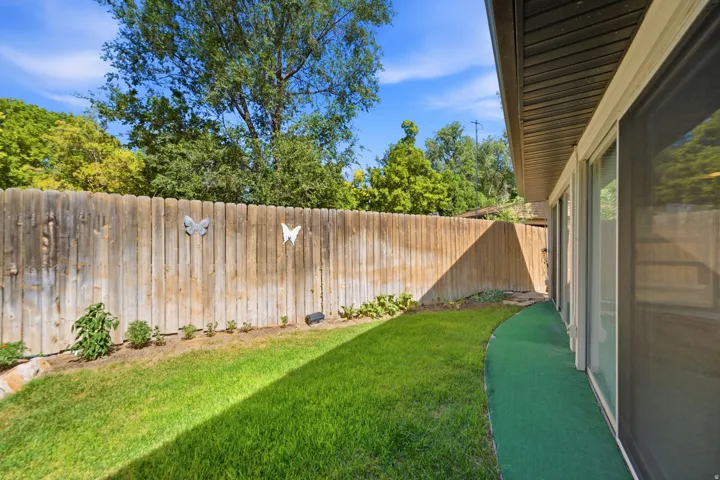 Private backyard with wood fencing, a grass lawn, and a paved pathway alongside the residence