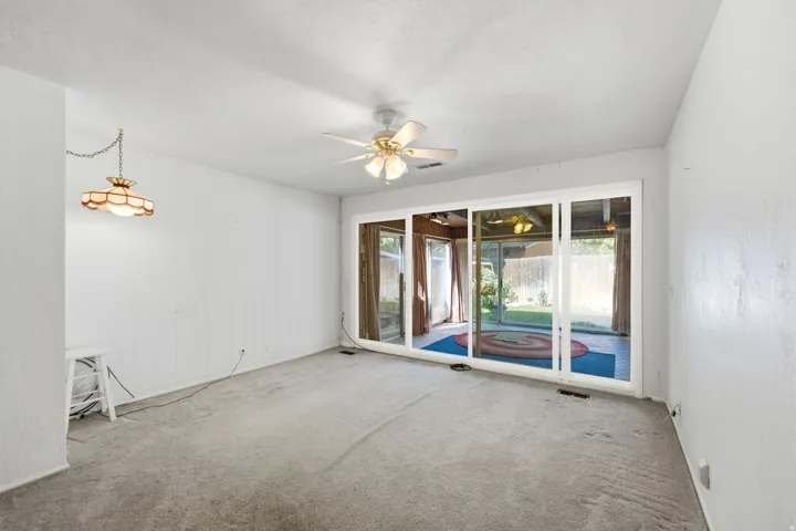 Sliding glass doors opening to the exterior, paneled accent wall, and a ceiling fan with integrated lighting