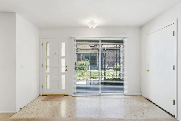 Entryway featuring light-toned flooring, a decorative front door with frosted glass panels, and a sliding glass door with blinds