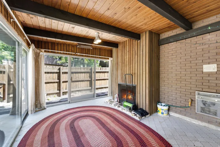 Exposed wood beam ceiling, wood plank wall paneling, brick accent wall, built-in fireplace, and sliding glass doors