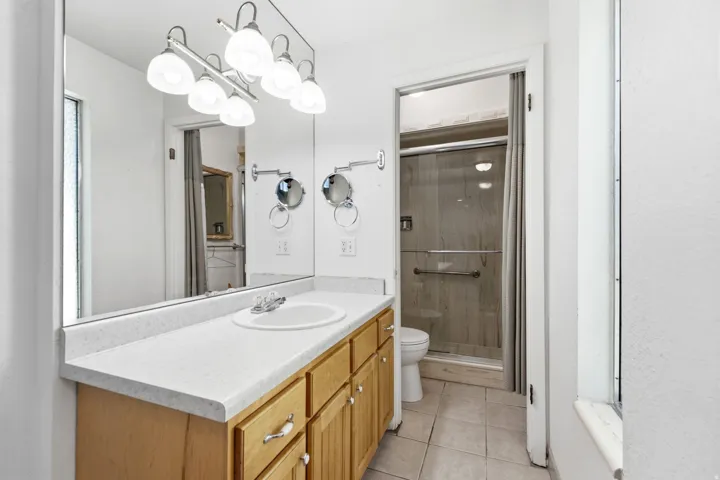 Vanity with light wood cabinetry and a white countertop, undermount sink, and a mirrored wall