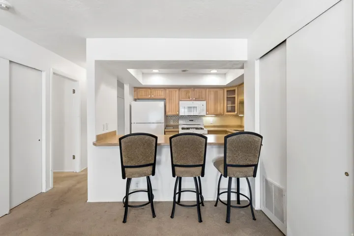Kitchen pass-through with a breakfast bar, wood-finish cabinetry, and white appliances