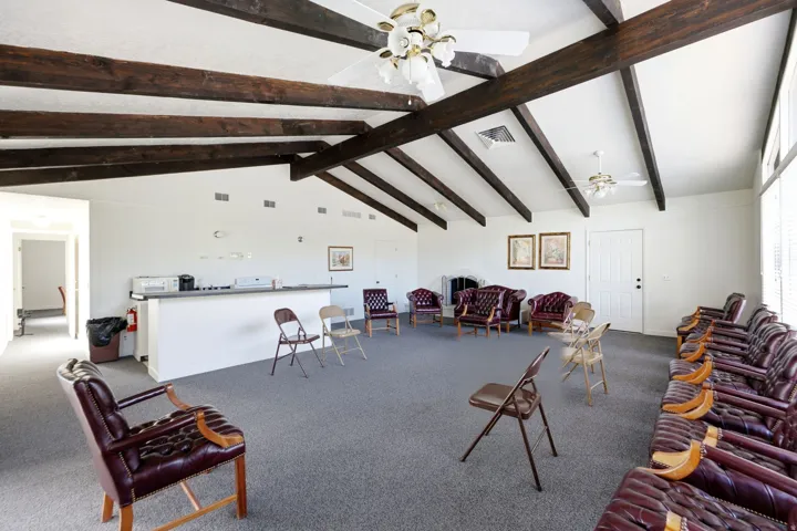 Vaulted ceiling with exposed wood beams, ceiling fans, built-in bar, wall-mounted fireplace, and expansive windows